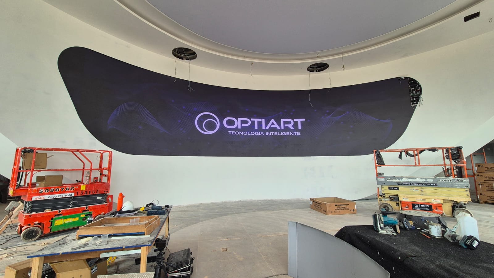 Painel de LED curvo ligado exibindo a logomarca da Optiart, embutido em parede branca no showroom da Denza em Brasília