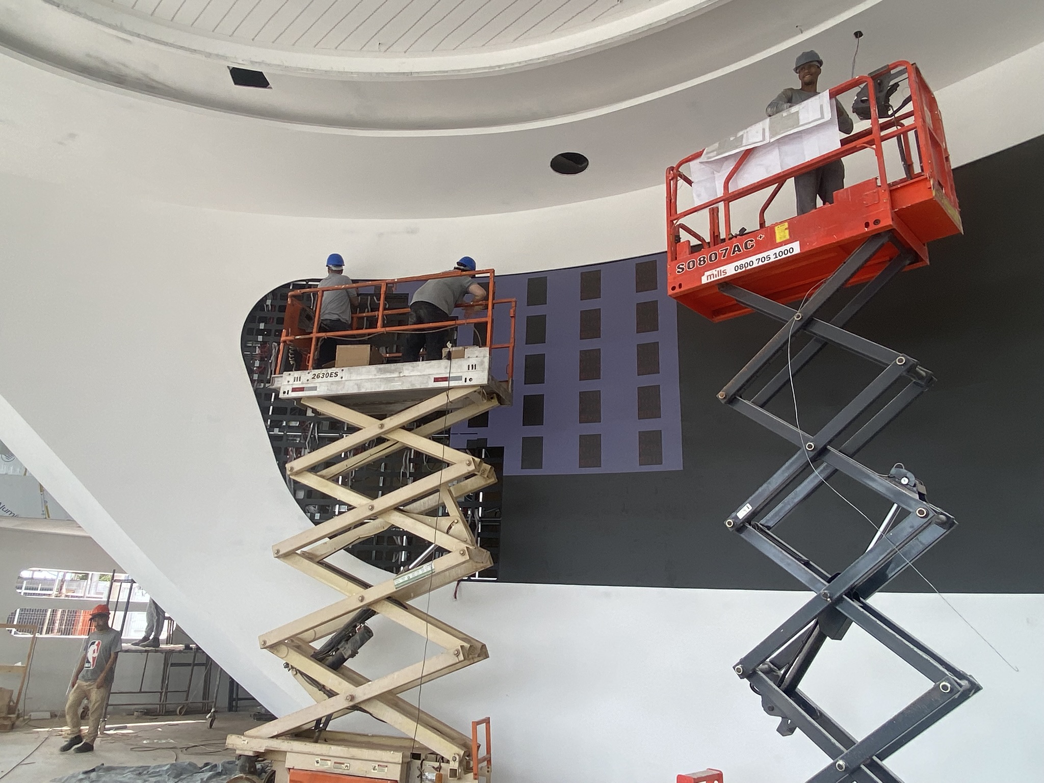 Técnicos em plataformas elevatórias instalando os módulos do painel de LED curvo