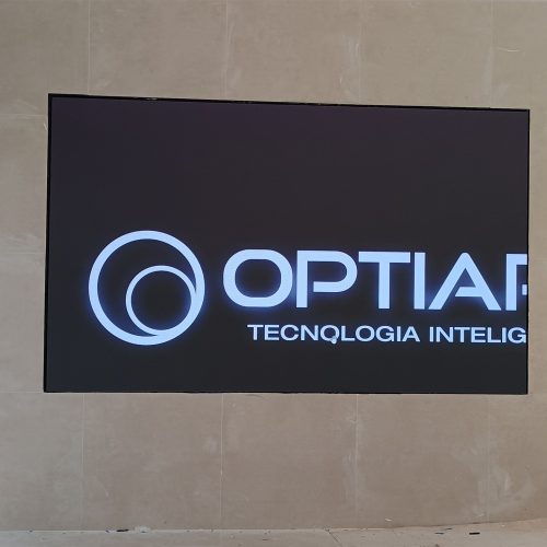 Painel de LED ligado exibindo a logomarca da Optiart, embutido em parede de porcelanato no showroom da Geely