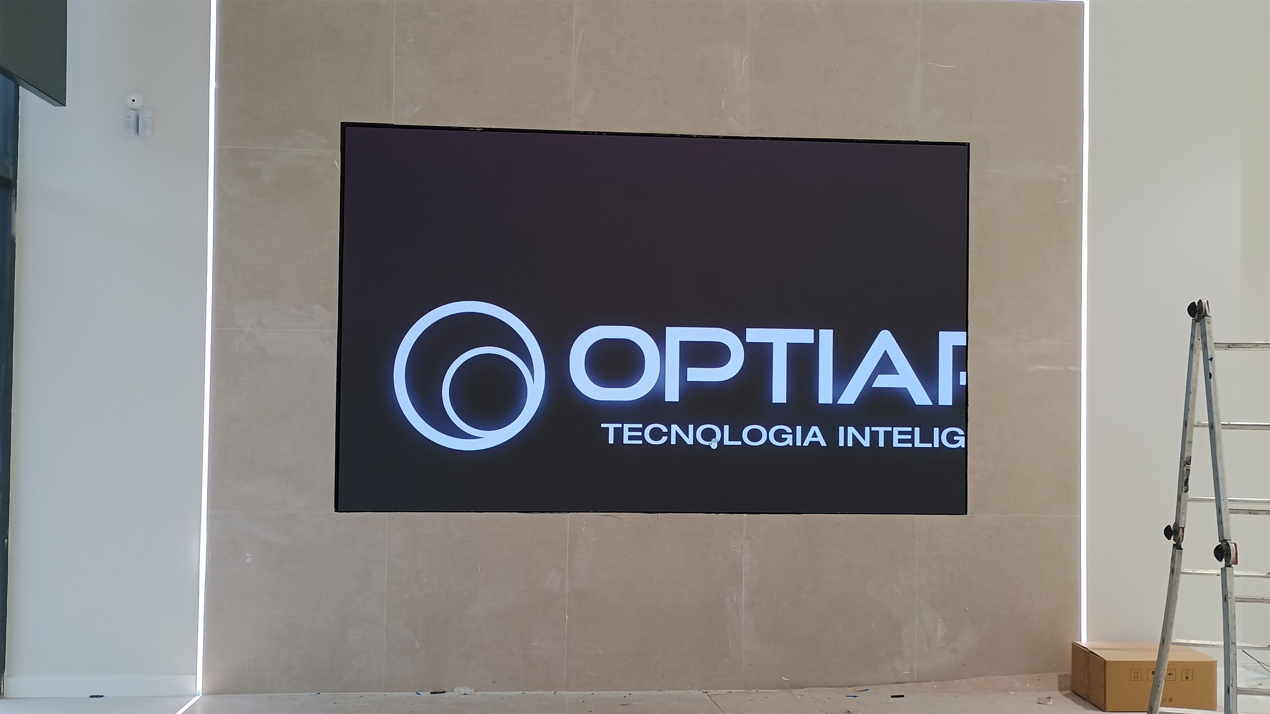 Painel de LED ligado exibindo a logomarca da Optiart, embutido em parede de porcelanato no showroom da Geely