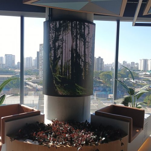 Painel de LED curvo envolvendo coluna cilíndrica em lounge corporativo em São Paulo, exibindo imagem de floresta