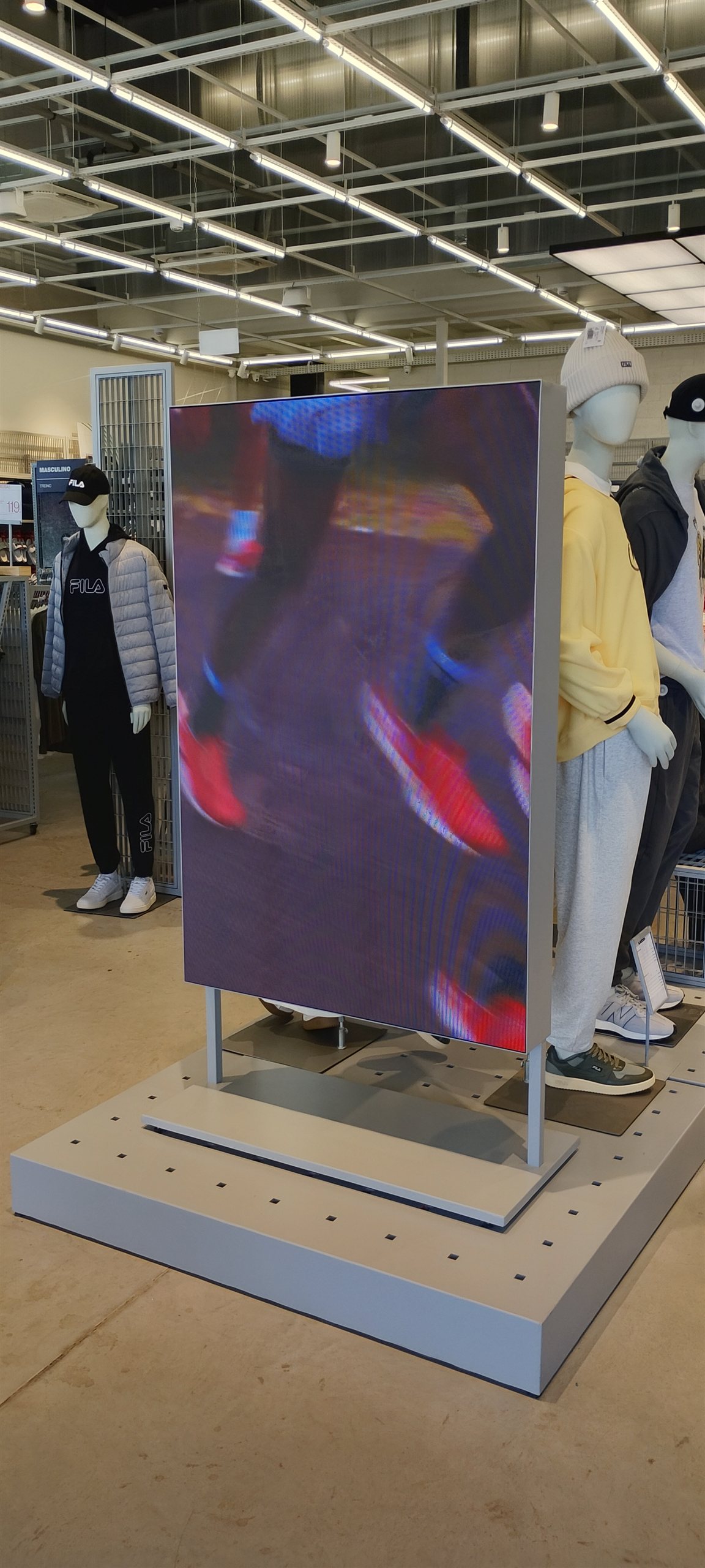 Painel de LED outdoor P4.0 em formato vertical exibindo conteudo colorido em area de vendas de loja de varejo
