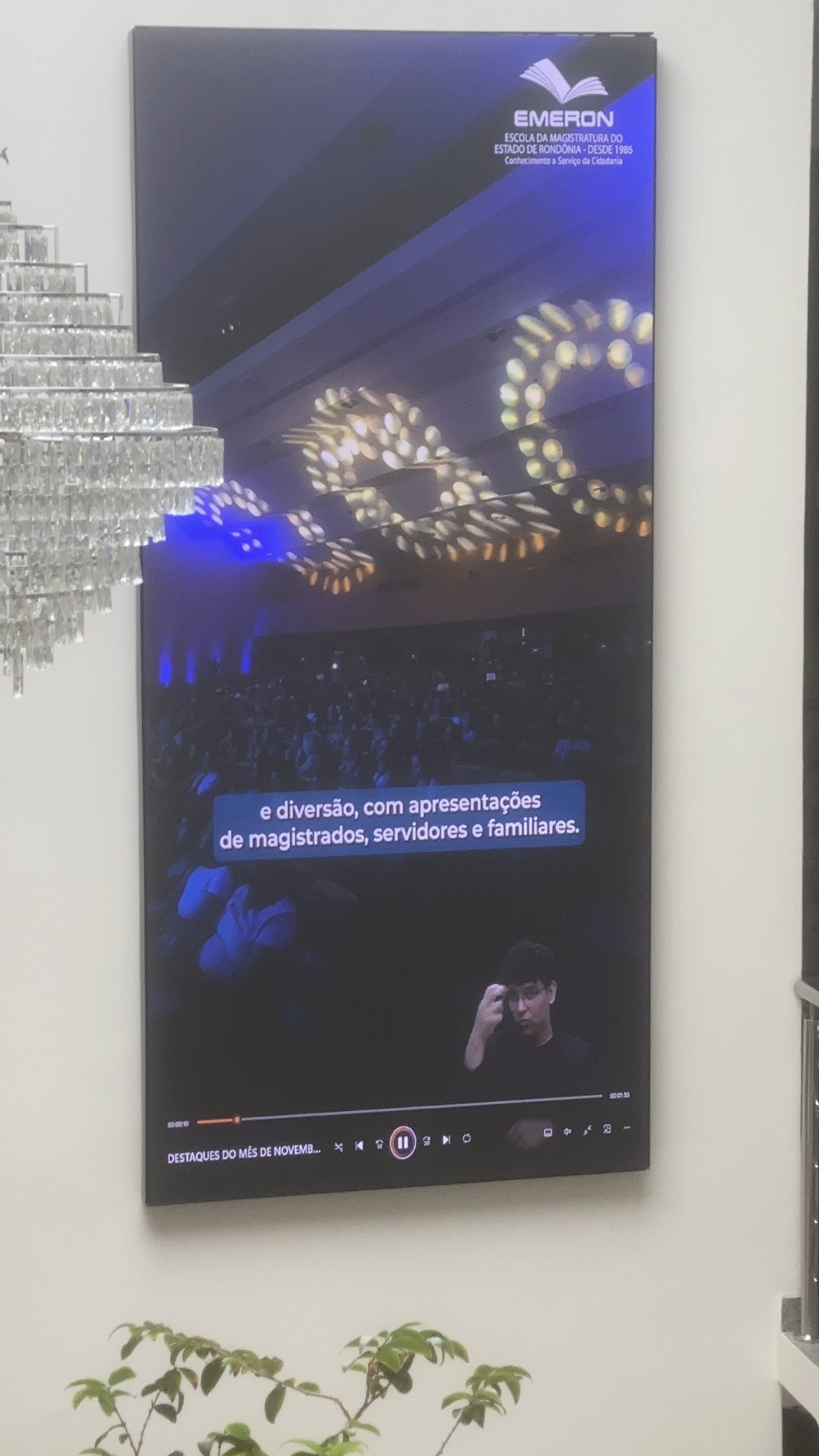 Painel de LED vertical exibindo vídeo institucional da mídia digital DOOH com legendas e intérprete de Libras