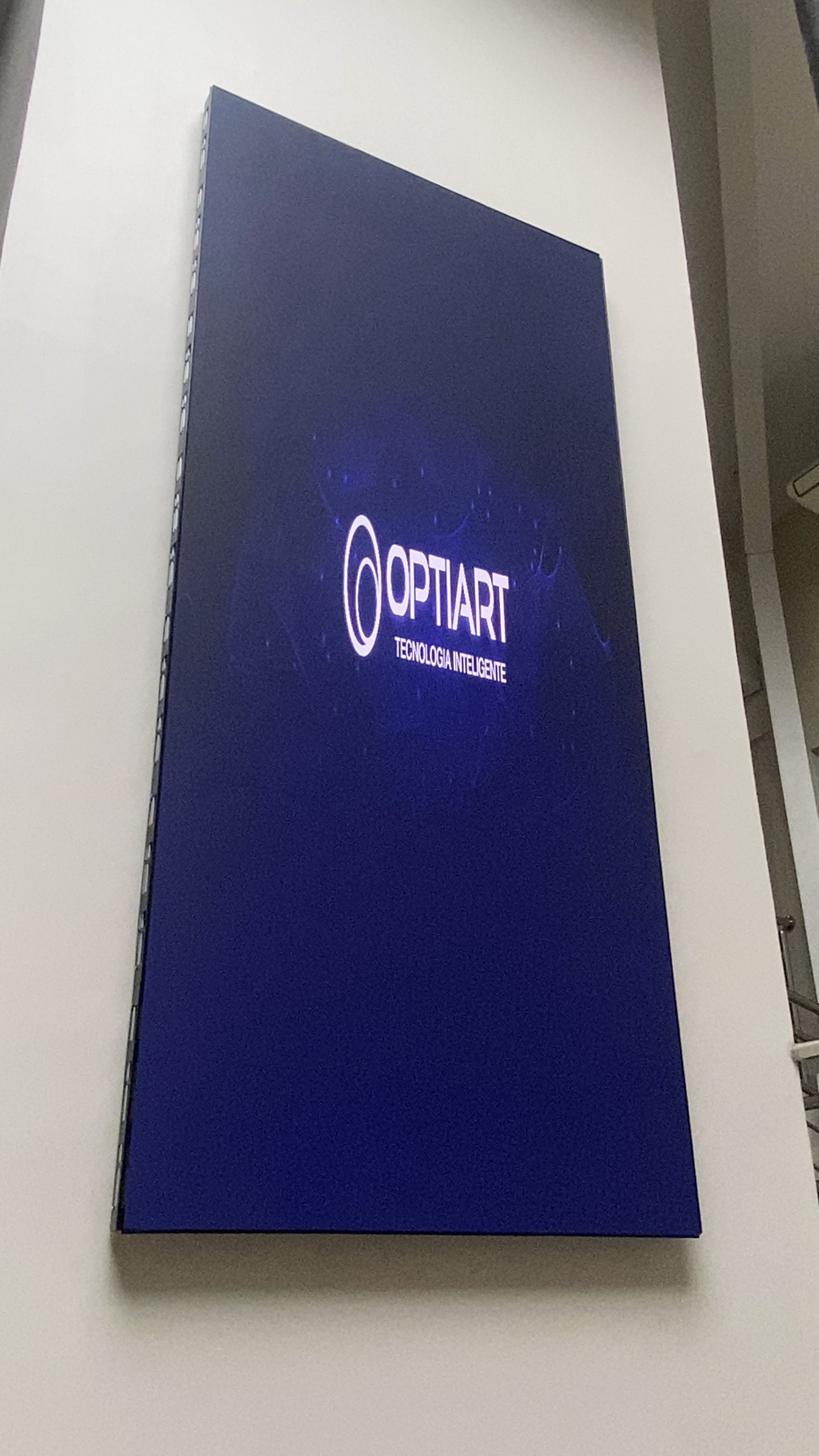 Painel de LED vertical ligado exibindo logotipo da Optiart em parede alta