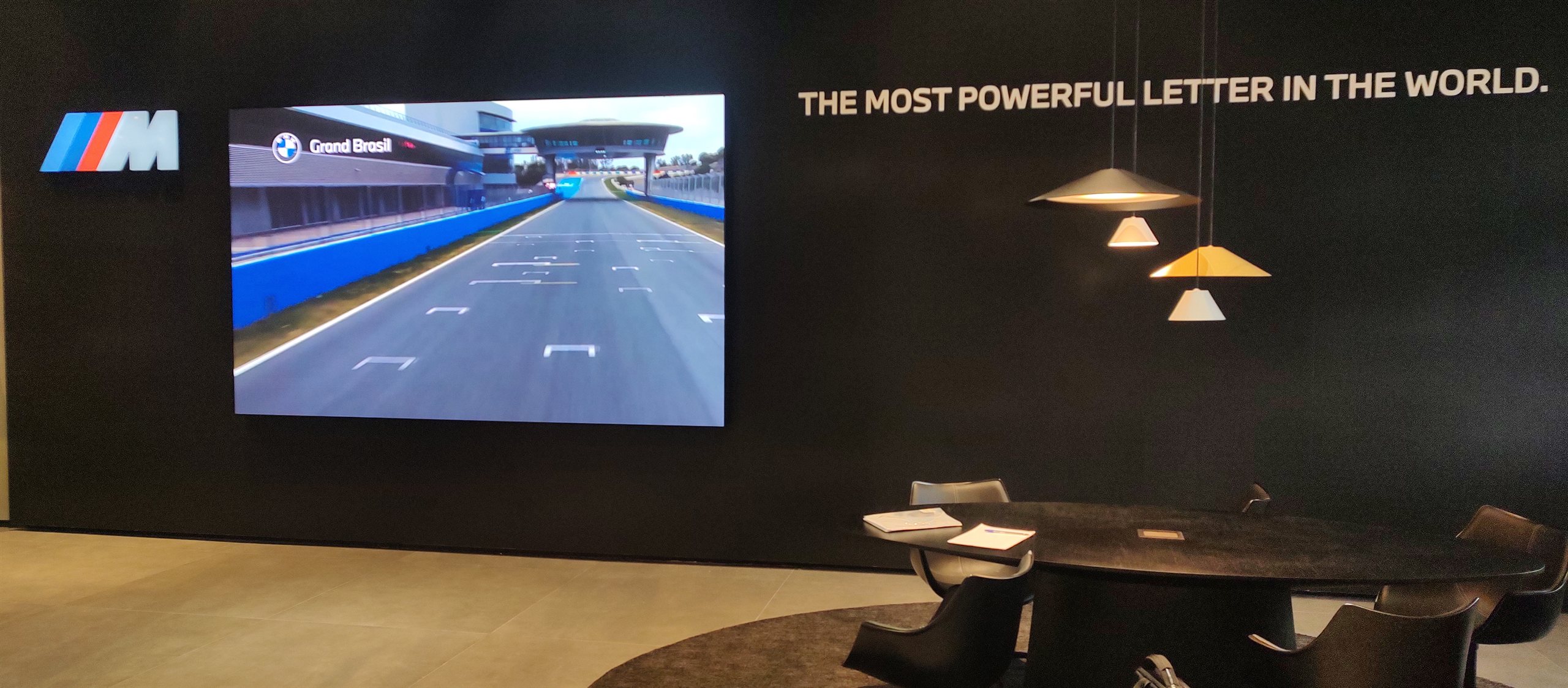 Painel de LED P2.5 instalado na concessionaria BMW Grand Brasil, exibindo conteudo da BMW M em um circuito de corrida, ao lado de lounge de atendimento