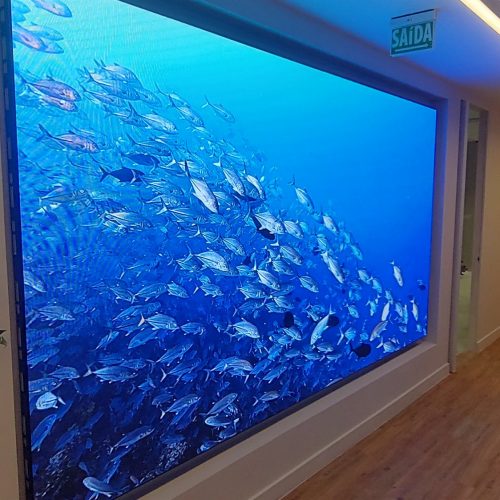 Painel de LED indoor P2.5 exibindo cena de aquario em hall corporativo, ao lado de jardim vertical