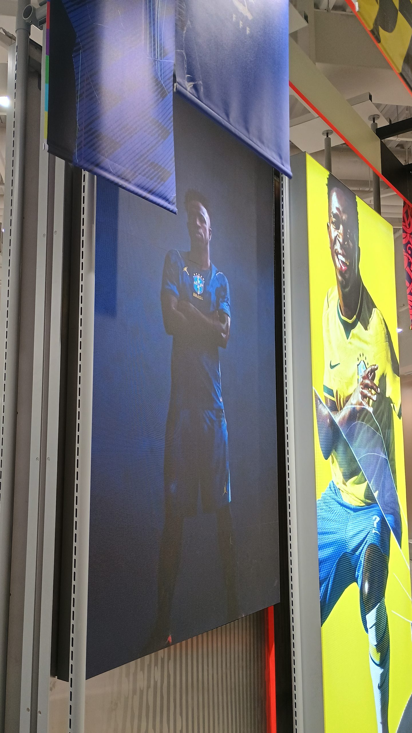 Dois painéis de LED em prateleiras de loja exibindo campanhas de futebol