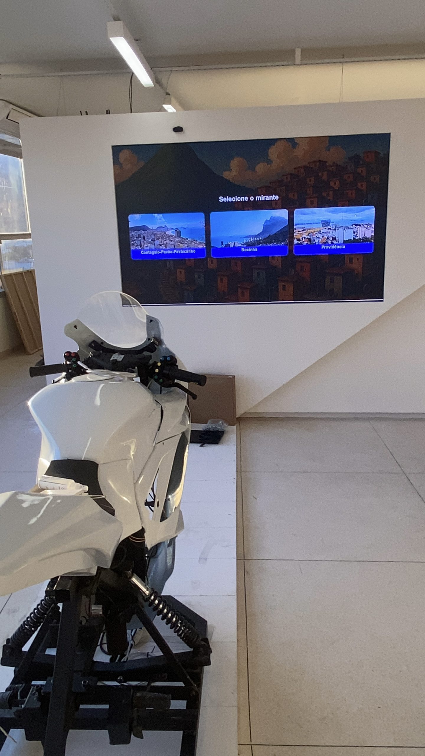 Simulador de moto em frente a painel de LED exibindo interface interativa de seleção de mirante