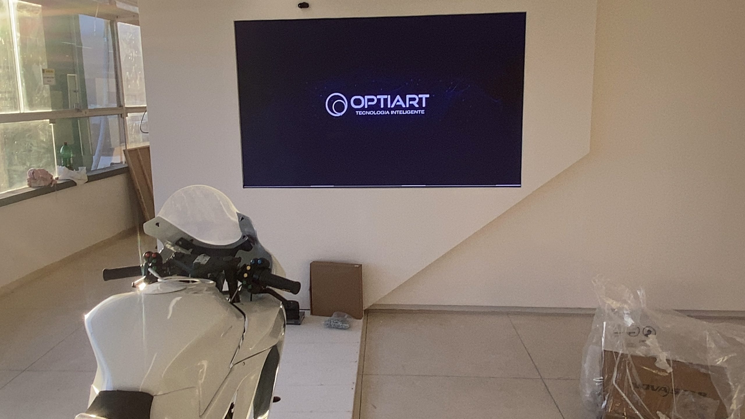 Painel de LED exibindo logotipo da Optiart com simulador de moto em primeiro plano no espaço expositivo