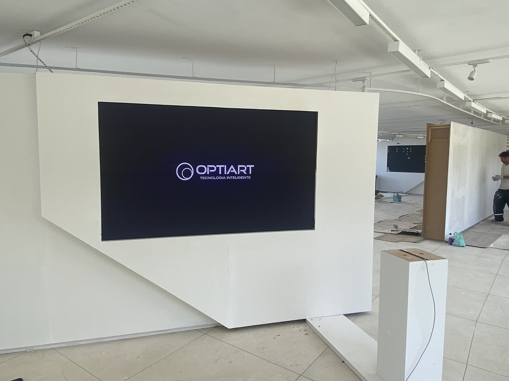 Painel de LED embutido em parede expositiva branca exibindo logotipo da Optiart