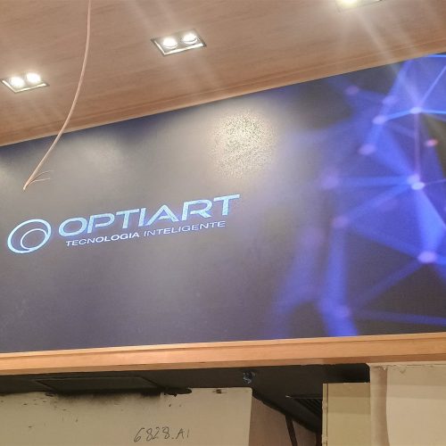 Painel de LED indoor P2.5 instalado em loja de shopping exibindo conteudo de marca sobre fundo azul, com moldura de madeira