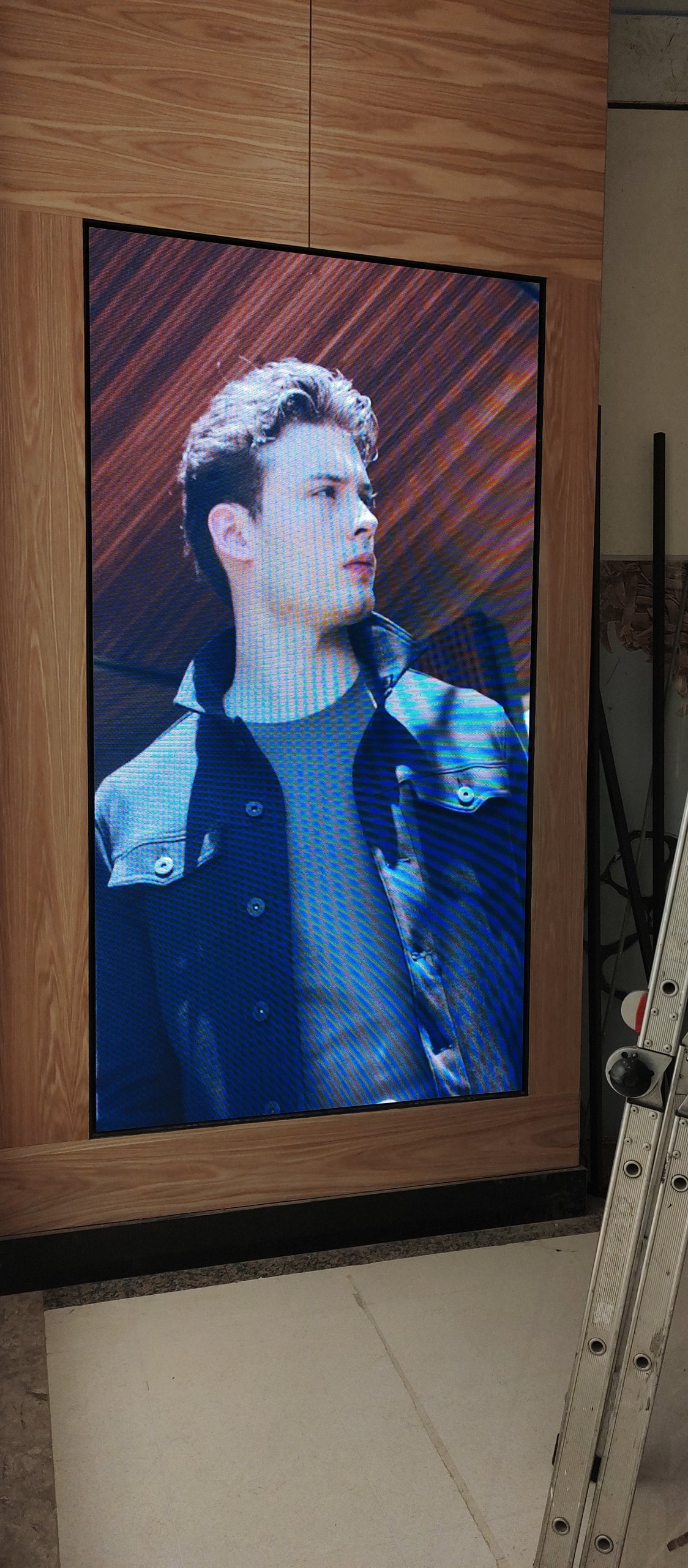 Painel de LED vertical instalado em moldura de madeira na loja Vila Romana com modelo de moda masculina