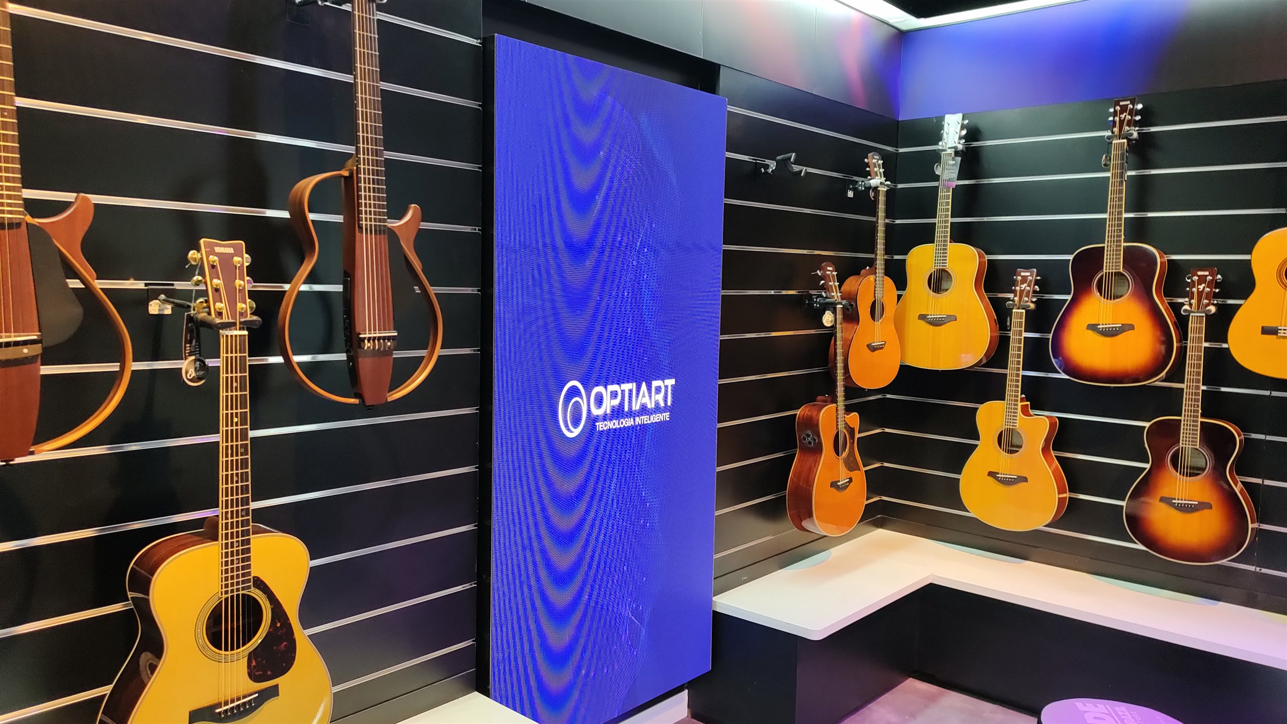 Painel de LED vertical em loja de instrumentos musicais Yamaha, cercado por violões em exposição na parede