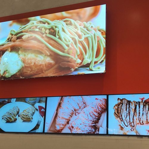 Painel de LED P2.5 exibindo produto da confeitaria acima do menu board de monitores na Carlo's Bakery Vila Leopoldina
