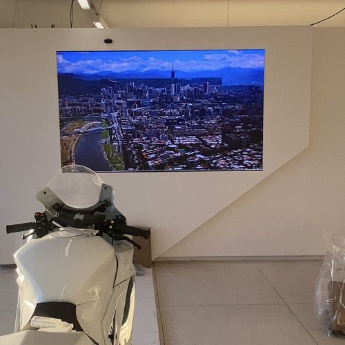 Painel de LED P1.8 embutido em parede cenográfica exibindo vídeo aéreo de cidade no Museu do Esporte, no Rio de Janeiro