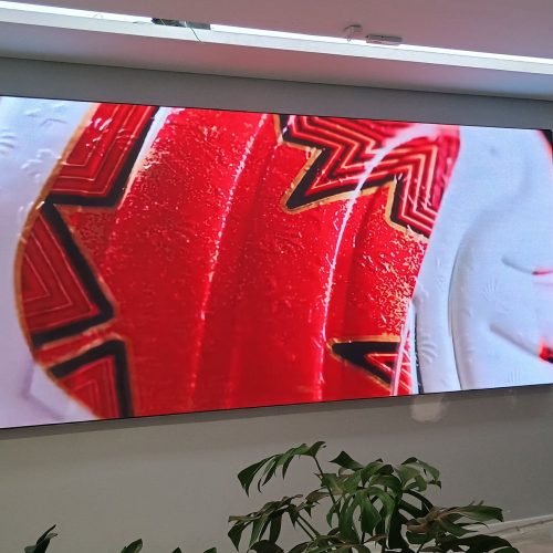 Painel de LED P1.8 panorâmico exibindo conteúdo em vermelho na parede da loja Centauro, com planta em primeiro plano