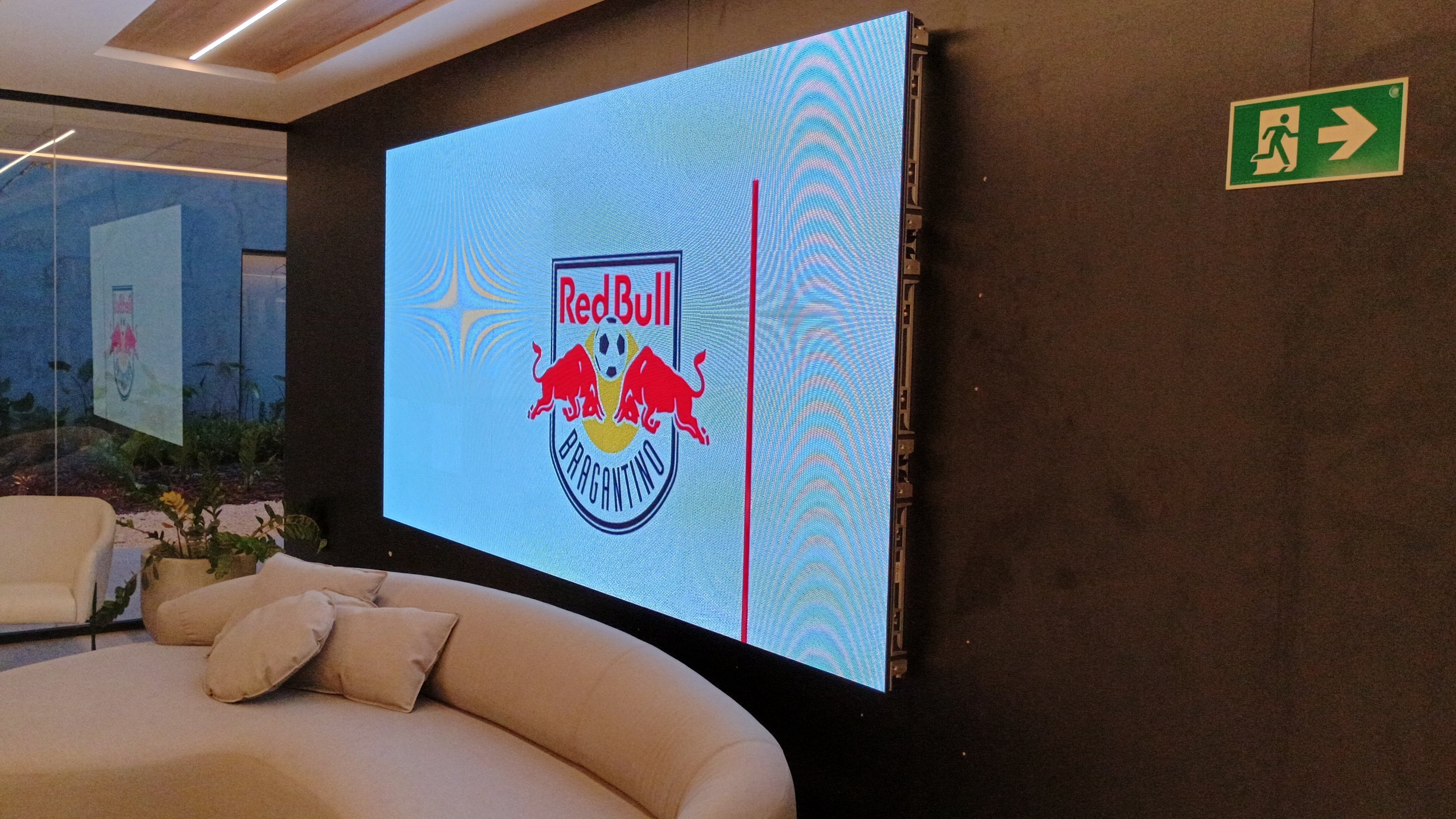 Painel de LED exibindo o escudo do Red Bull Bragantino na recepcao com sofa curvo