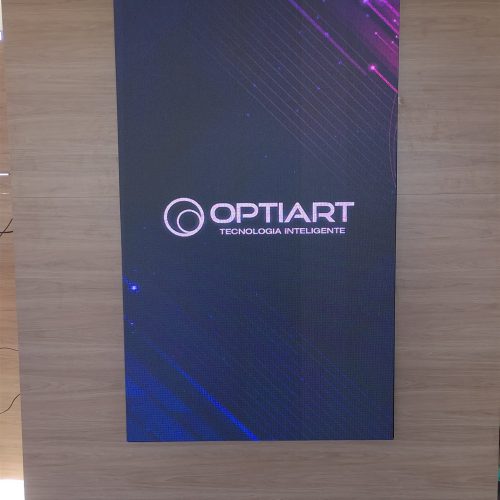 Painel de LED vertical P2.5 instalado sobre parede de madeira em ambiente corporativo