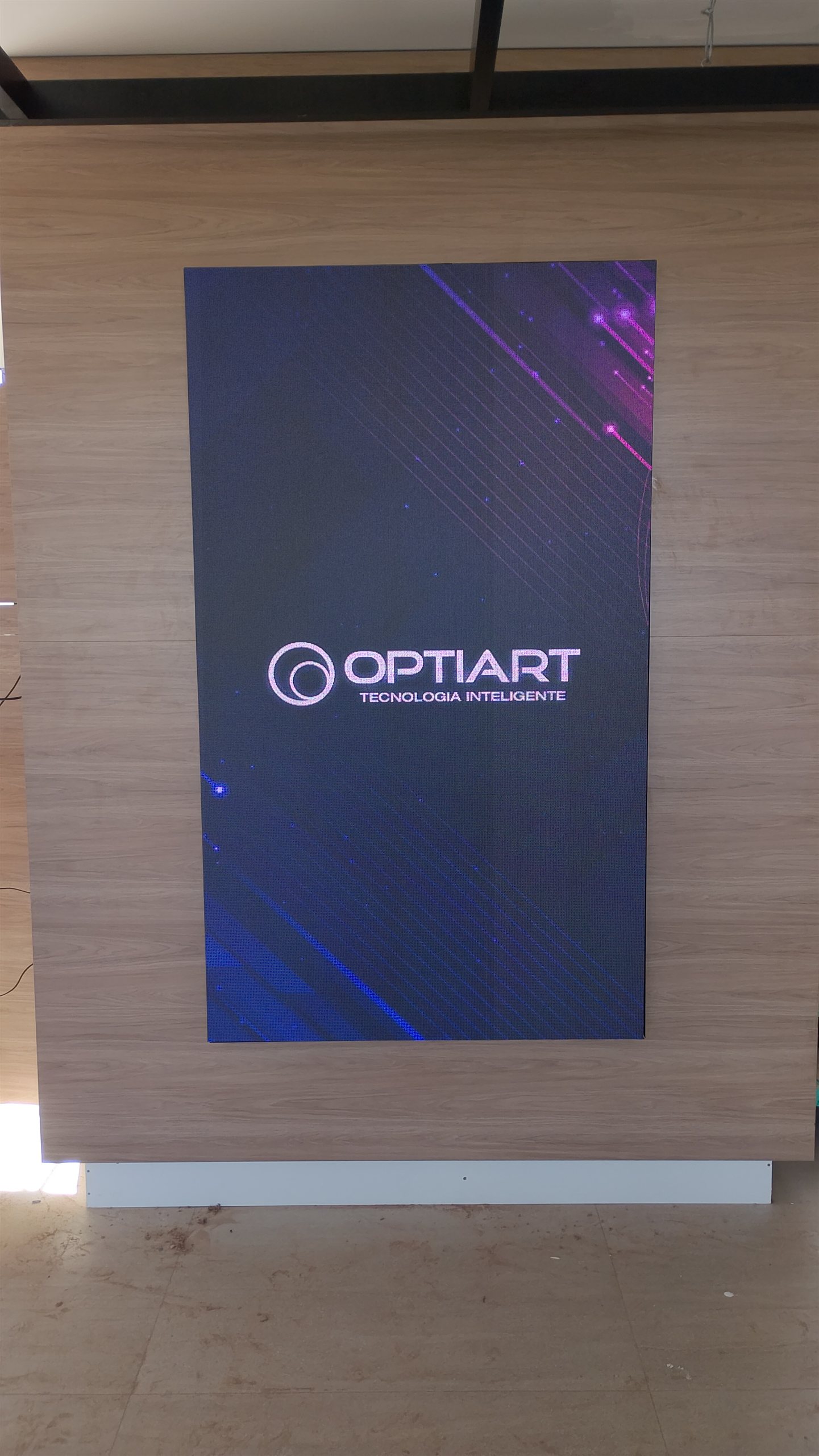 Painel de LED vertical P2.5 instalado sobre parede de madeira em ambiente corporativo