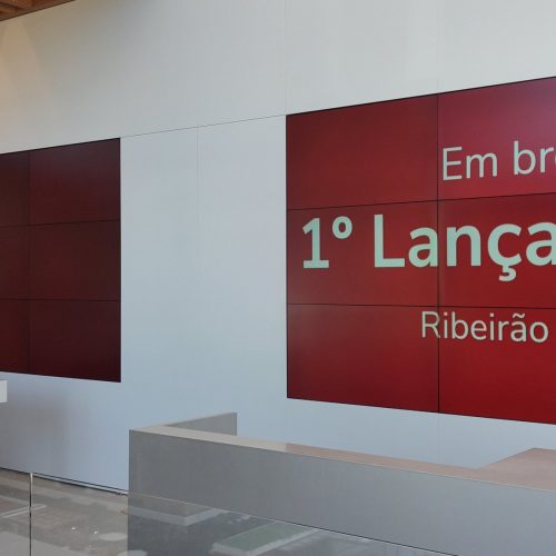 Dois videowalls 3x3 instalados no mesmo hall do stand de vendas de uma incorporadora, um deles exibindo a chamada do lançamento imobiliário
