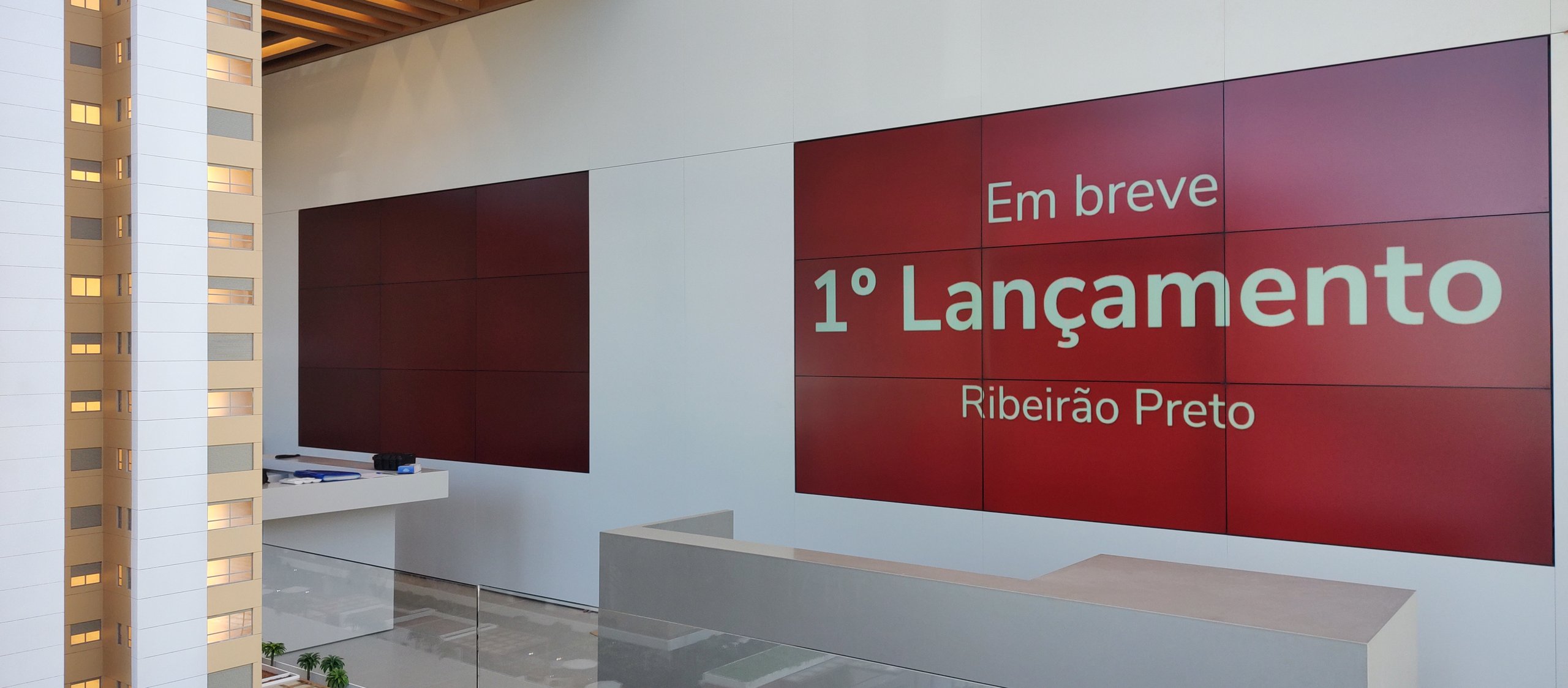 Dois videowalls 3x3 instalados no mesmo hall do stand de vendas de uma incorporadora, um deles exibindo a chamada do lançamento imobiliário
