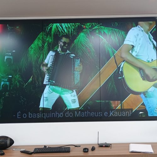 VideoWall 1x3 com três monitores verticais embutidos em nicho exibindo vídeo em tela cheia na recepção da Prudential em Goiânia, com frase institucional na parede ao lado