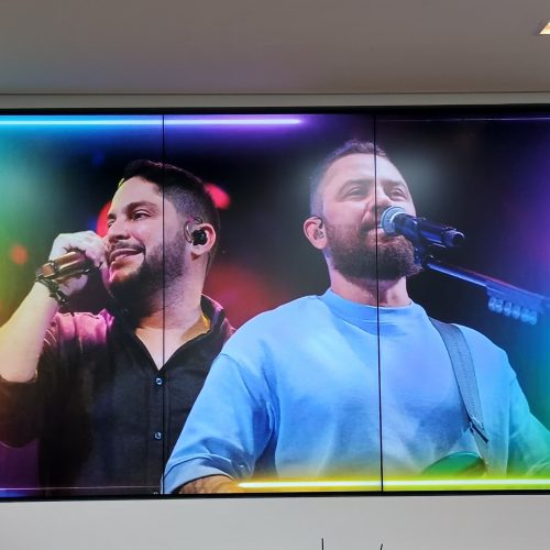 VideoWall 1x3 vertical embutido em nicho exibindo vídeo de show em tela cheia na agência Prudential Arrows em Goiânia, com frase institucional na parede