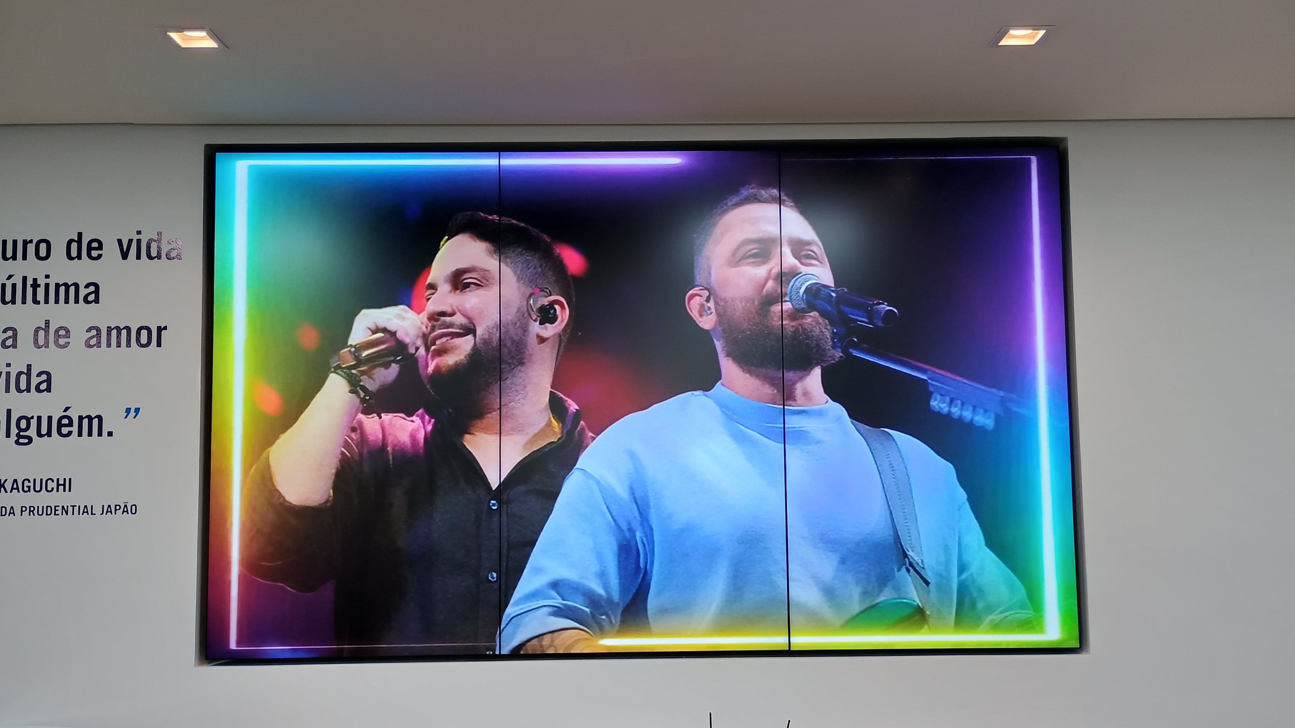 VideoWall 1x3 vertical embutido em nicho exibindo vídeo de show em tela cheia na agência Prudential Arrows em Goiânia, com frase institucional na parede