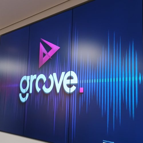 VideoWall 1x3 vertical embutido em nicho exibindo arte da marca Groove em tons de azul e rosa, no escritorio da Prudential Groove em Sao Jose dos Campos