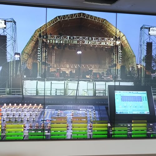 VideoWall 1x3 vertical com tres monitores em retrato exibindo imagem de palco de show, instalado em parede de escritorio corporativo da Prudential Guardians em Recife