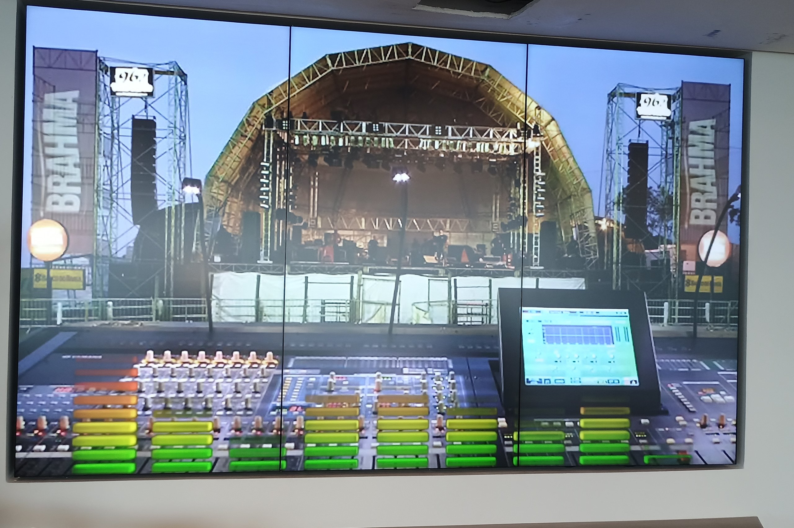 VideoWall 1x3 vertical com tres monitores em retrato exibindo imagem de palco de show, instalado em parede de escritorio corporativo da Prudential Guardians em Recife