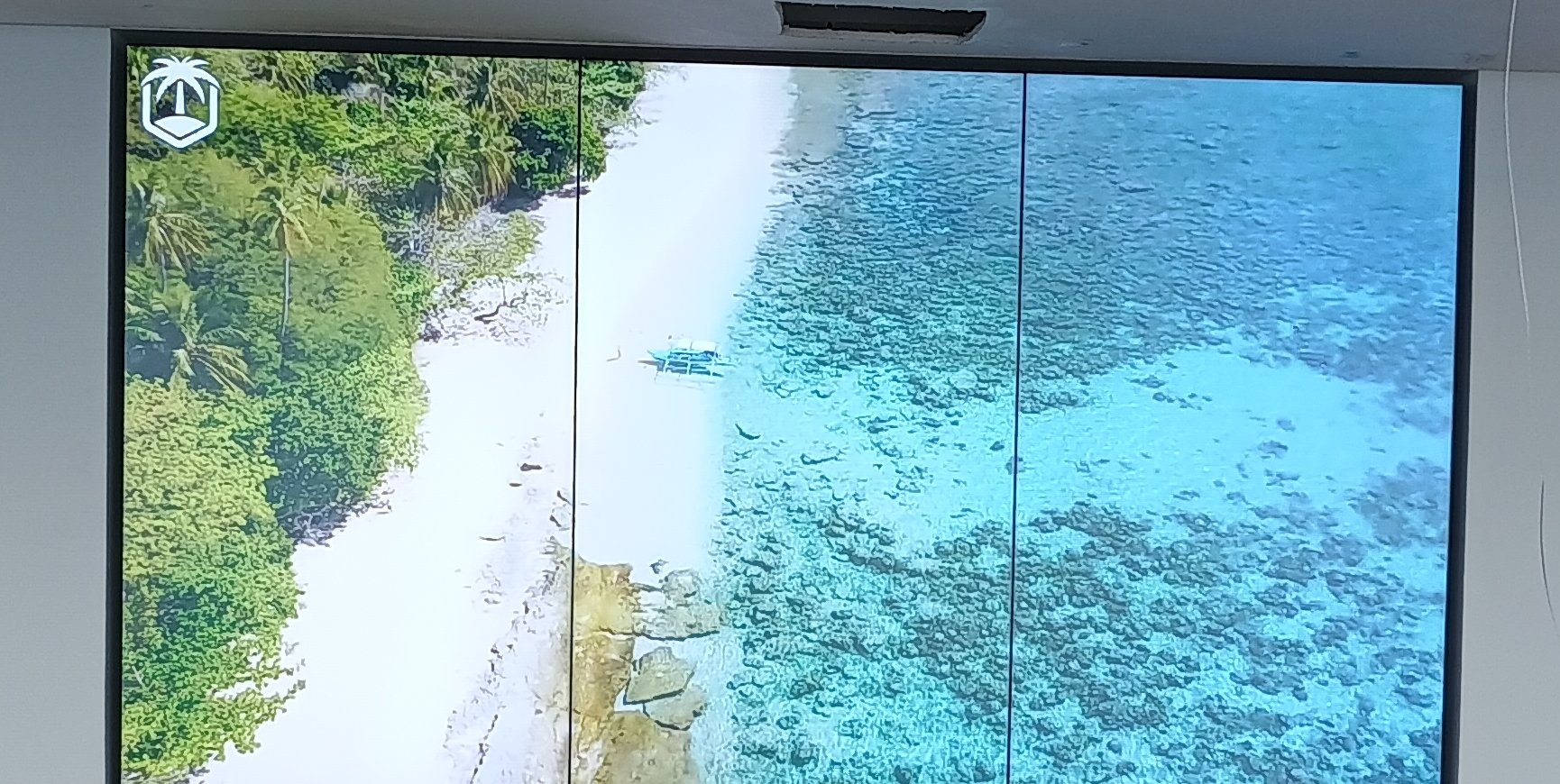 Detalhe do VideoWall 1x3 vertical exibindo imagem aerea de praia com mar e vegetacao, tres telas em retrato lado a lado com bordas finas