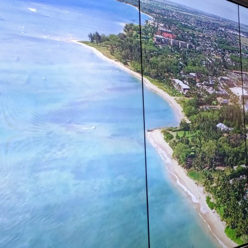 VideoWall 1x3 vertical em close exibindo imagem aerea de litoral com praia e cidade, tres telas em retrato com bordas finas, no escritorio da Prudential Marines em Recife