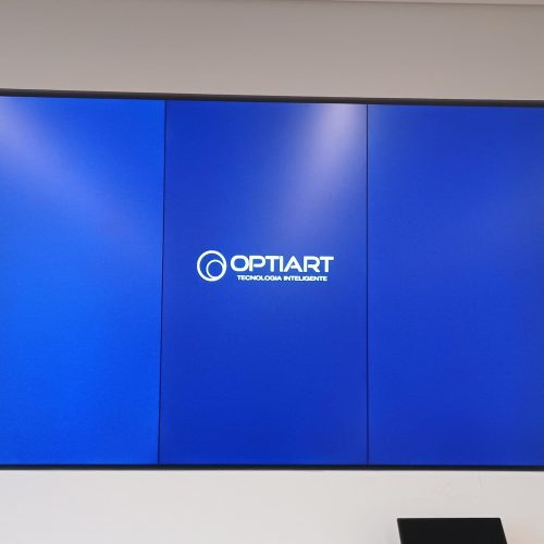 VideoWall 1x3 vertical embutido em nicho exibindo tela azul com logotipo da Optiart em escritório da Prudential Titanium em São Paulo