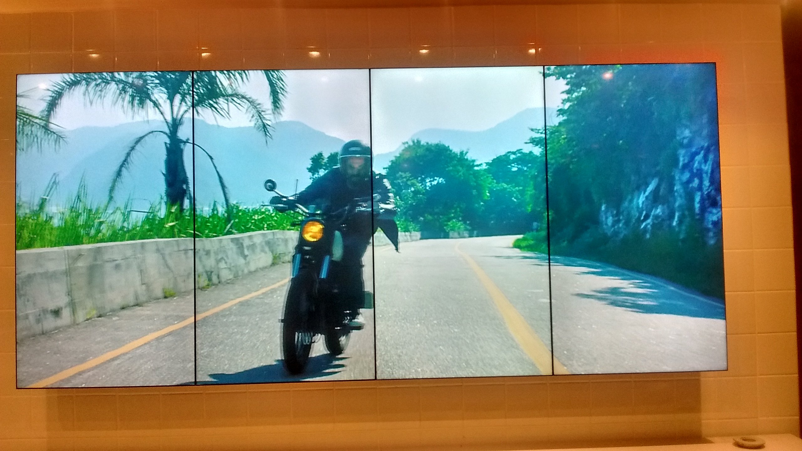 VideoWall 1x4 vertical na Foxton Rio Design Barra exibindo vídeo de motociclista em tela cheia