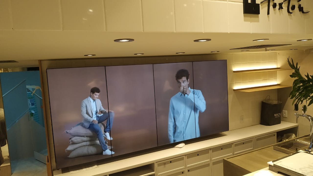 VideoWall de quatro telas verticais lado a lado exibindo modelos da coleção Foxton acima do mobiliário da loja