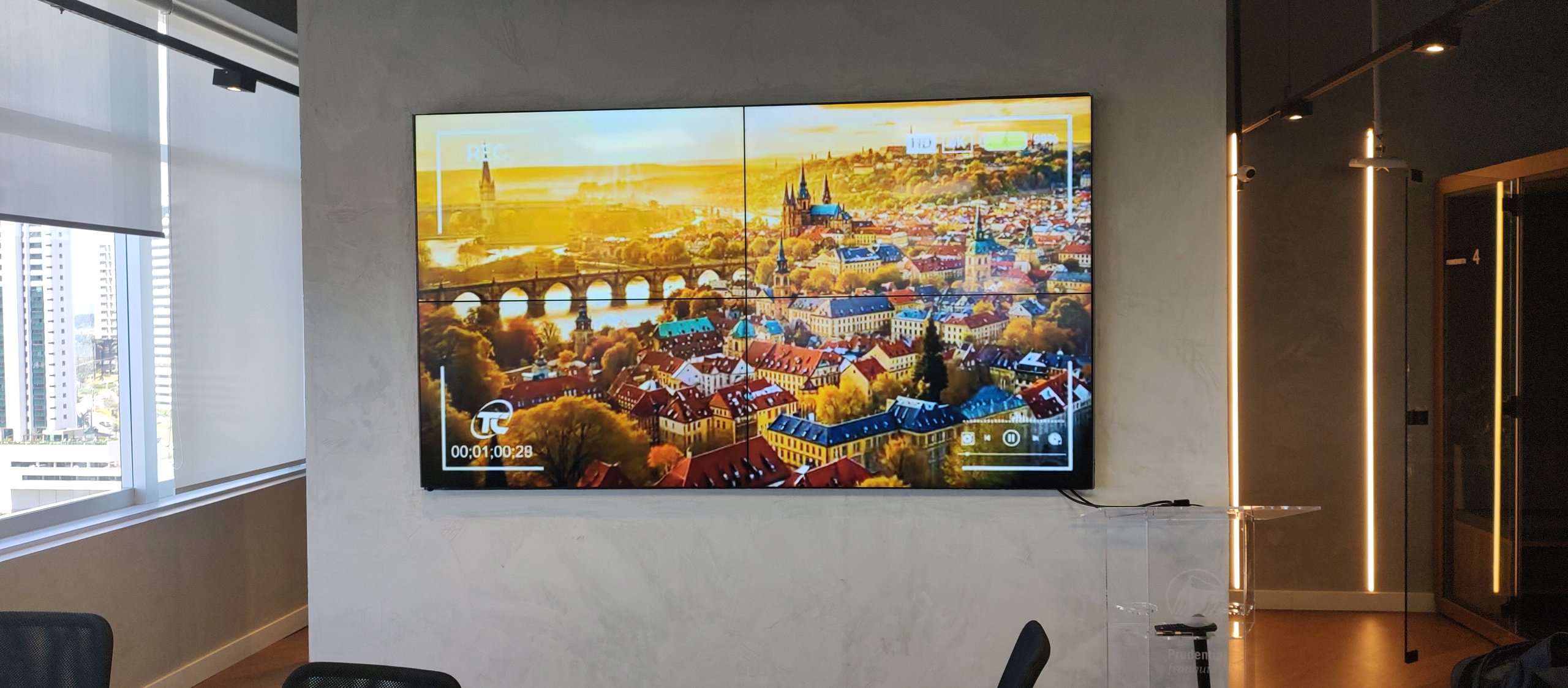Sala da agência Prudential Star em Nova Lima com VideoWall 2x2 exibindo vídeo de paisagem urbana em tela cheia