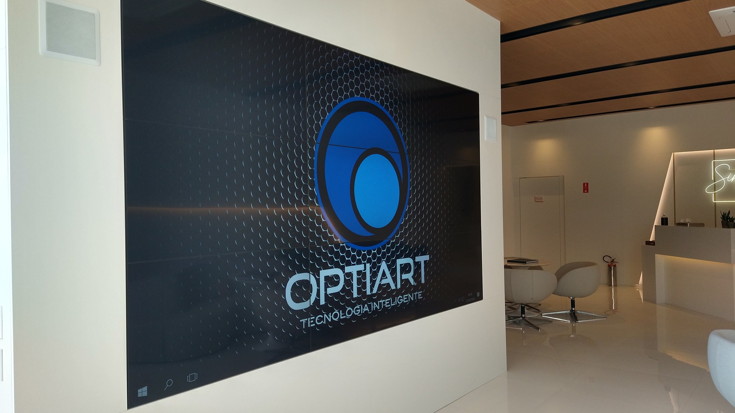 VideoWall 3x3 ligado na recepção do estande de vendas, com balcão de atendimento e poltronas ao fundo