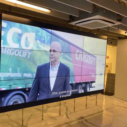 VideoWall 3x3 com as nove telas ligadas exibindo um vídeo institucional no hall corporativo da TOTVS