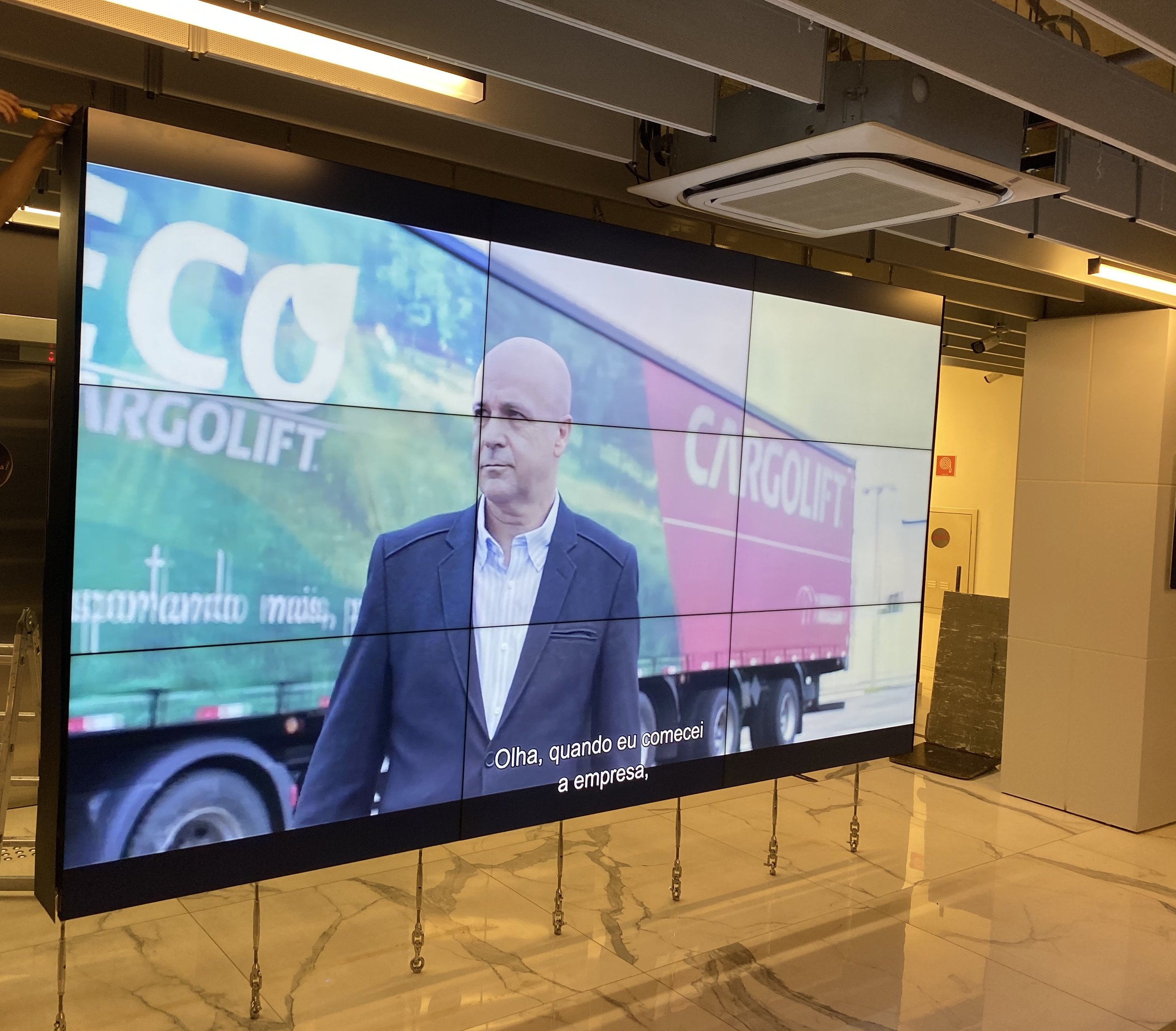 VideoWall 3x3 com as nove telas ligadas exibindo um vídeo institucional no hall corporativo da TOTVS