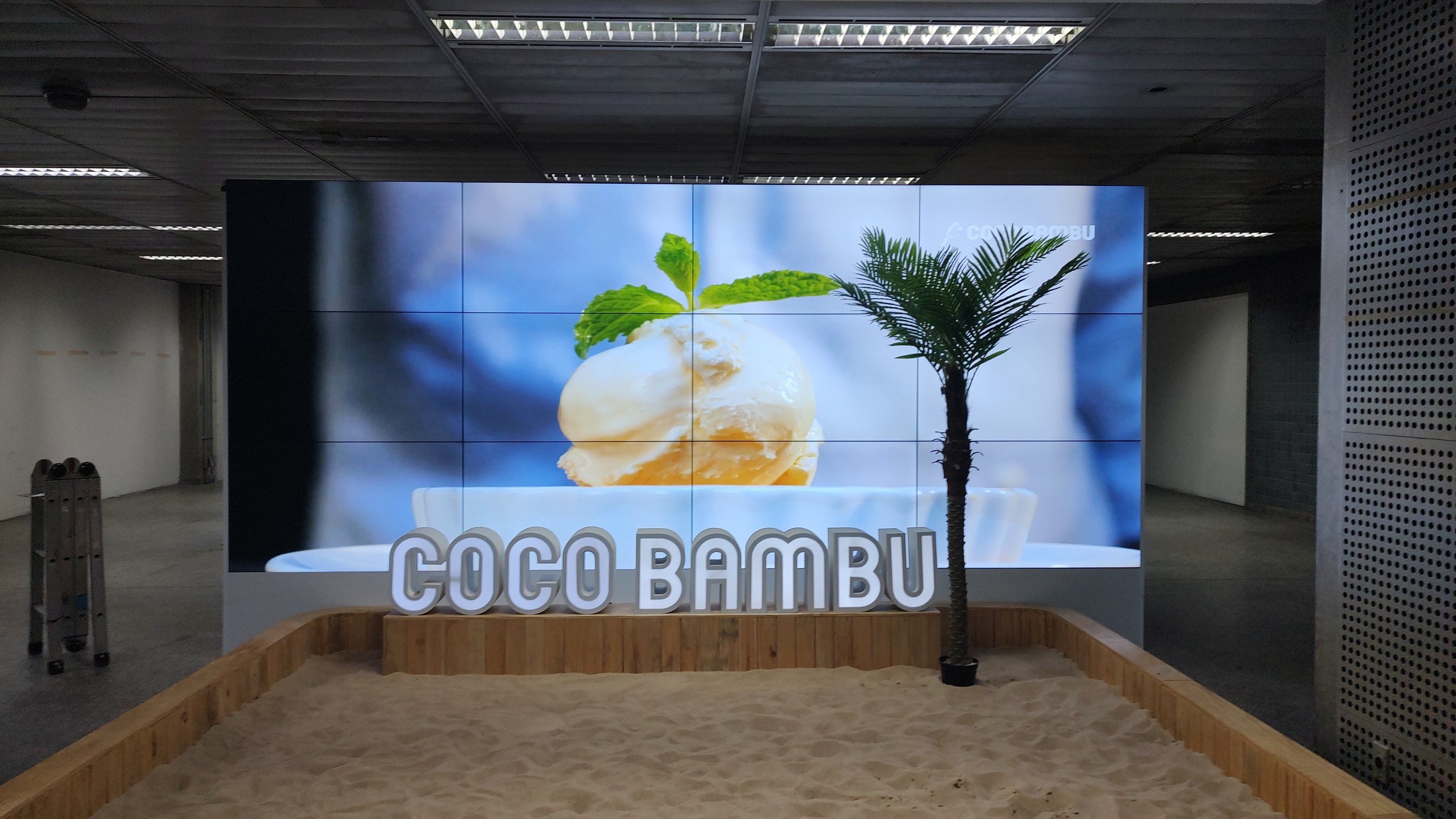 VideoWall 3x4 do Coco Bambu no Aeroporto de Guarulhos exibindo imagem de sobremesa, com letreiro Coco Bambu à frente
