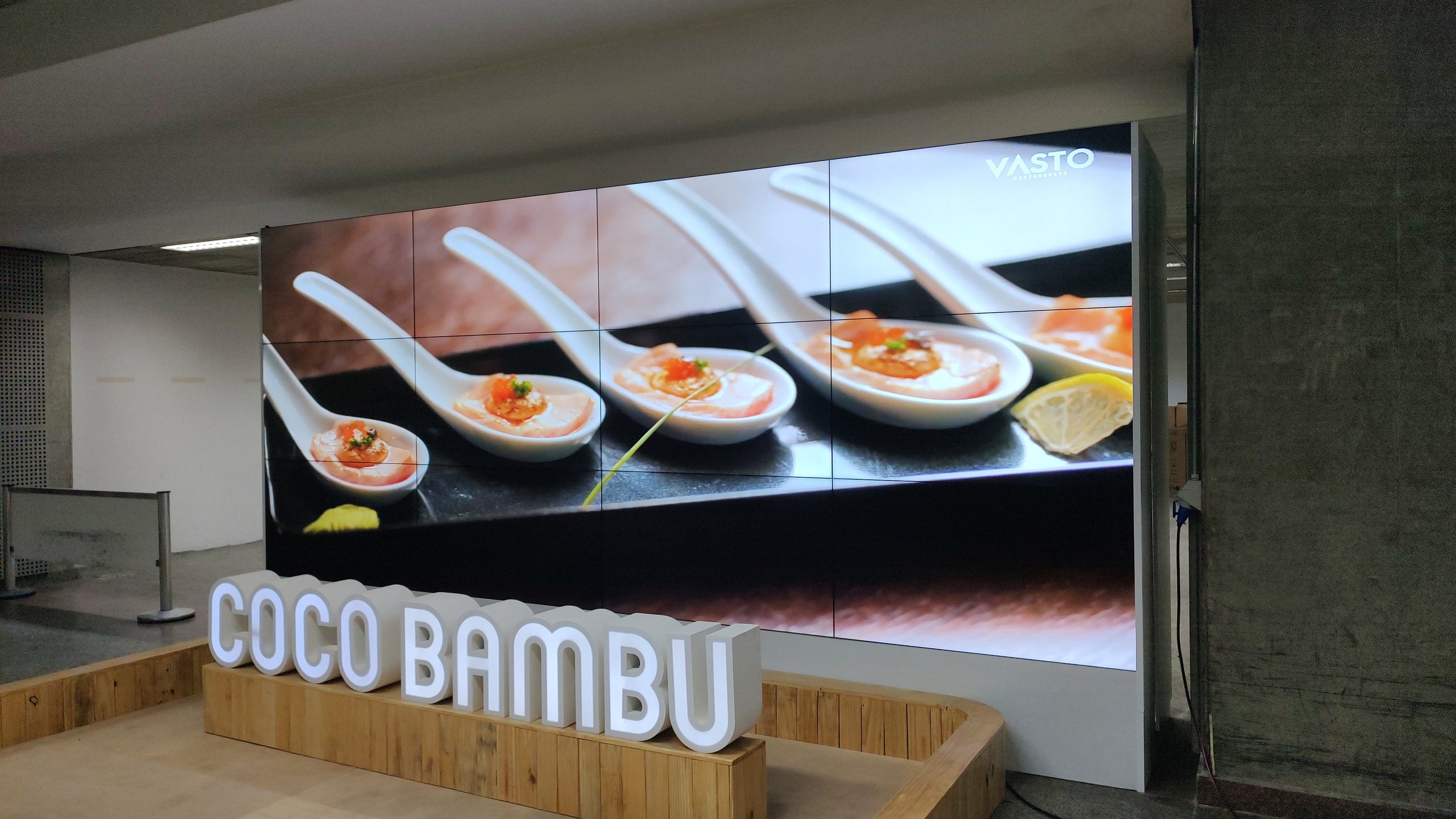 VideoWall 3x4 em ângulo mostrando conteúdo gastronômico e a marca VASTO Restaurantes no quiosque do aeroporto