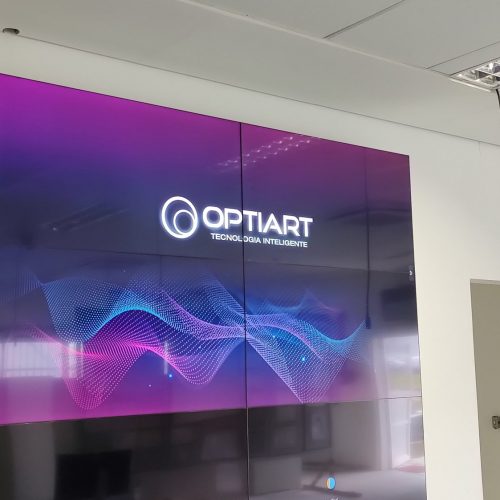 VideoWall 3x4 em sala de controle industrial com quatro telas exibindo a identidade visual da Optiart