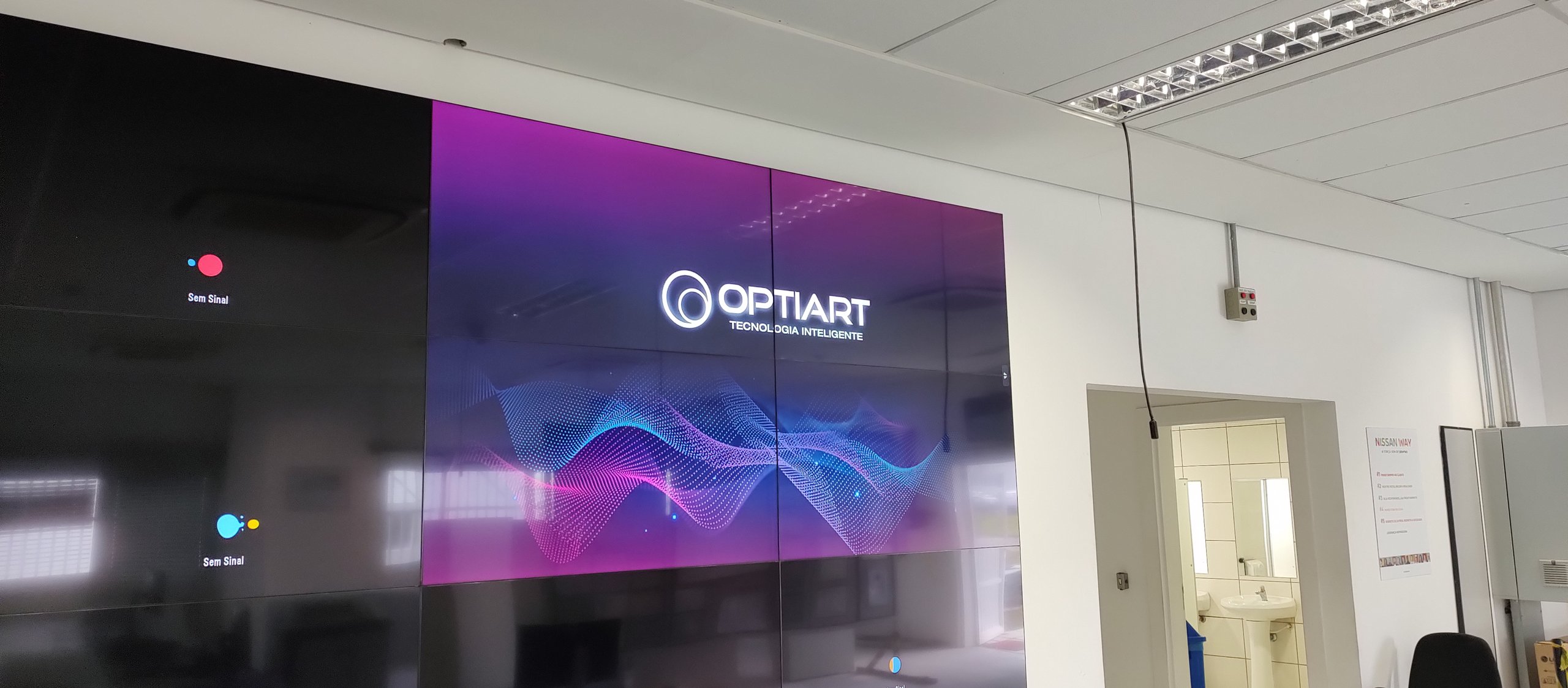VideoWall 3x4 em sala de controle industrial com quatro telas exibindo a identidade visual da Optiart