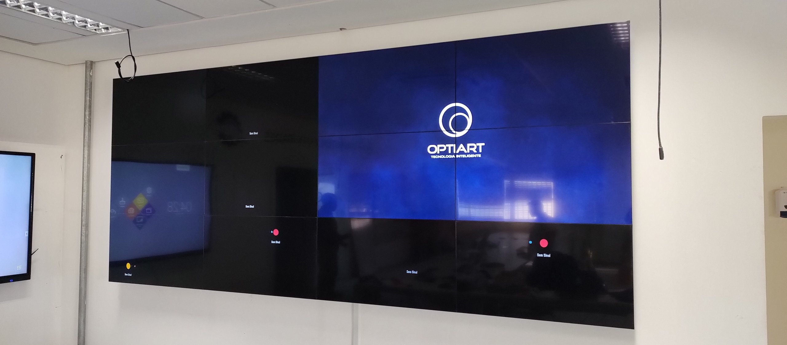 VideoWall 3x4 instalado sobreposto à parede da sala de monitoramento, com parte das telas em exibição