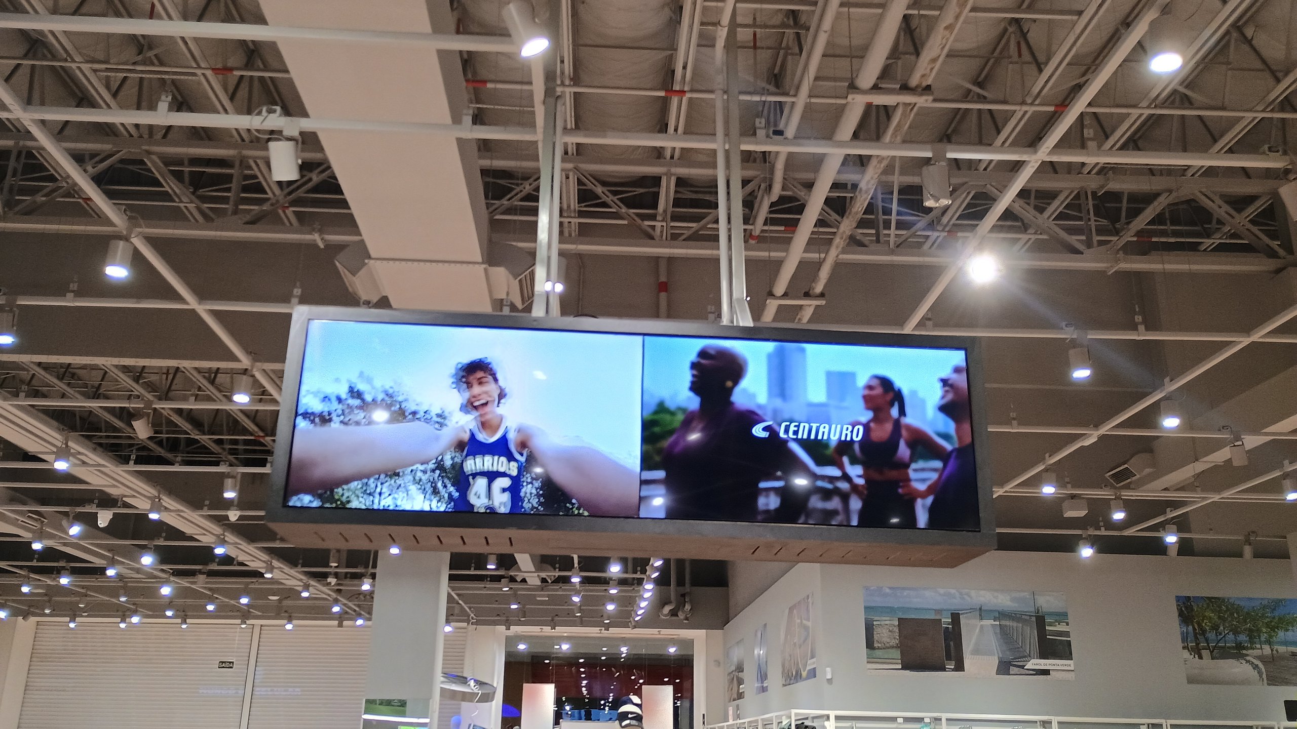 Videowall suspenso ligado exibindo campanha da Centauro sobre o salão da loja