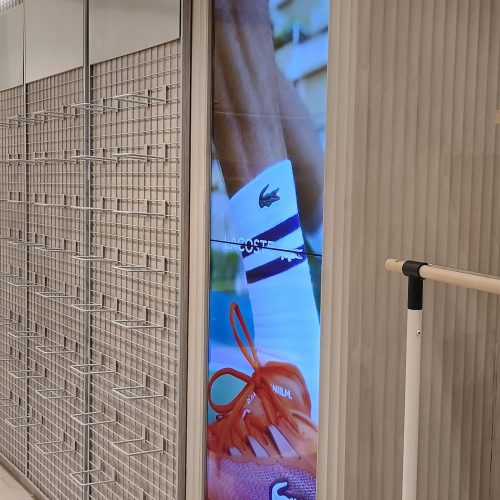 VideoWall vertical com dois monitores LG 49 polegadas exibindo campanha de tênis em loja Lacoste em Londrina