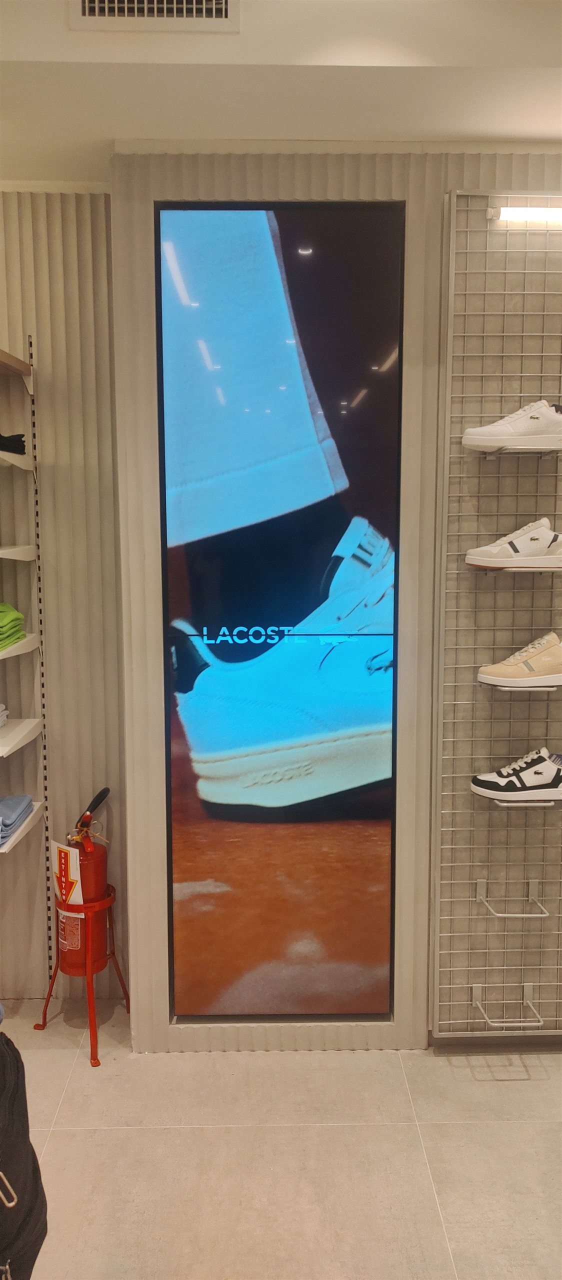 Coluna de VideoWall embutida na marcenaria exibindo campanha de tênis Lacoste ao lado do expositor de calçados