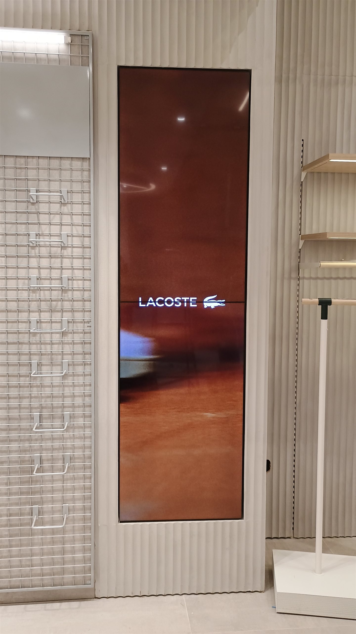 Coluna digital vertical embutida na marcenaria exibindo a marca Lacoste em loja de Londrina